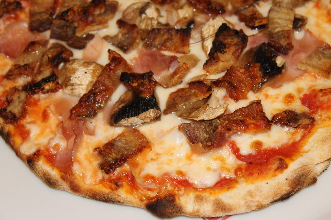 Pizza Teo recién salida del horno, con panceta, jamón y champiñones
